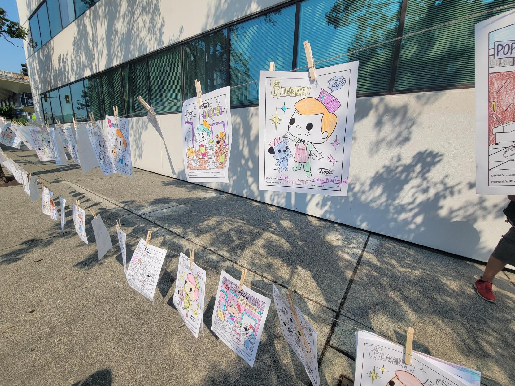 Coloring Pages: Various coloring pages hang on display in the street. The coloring pages feature Freddy Funko.